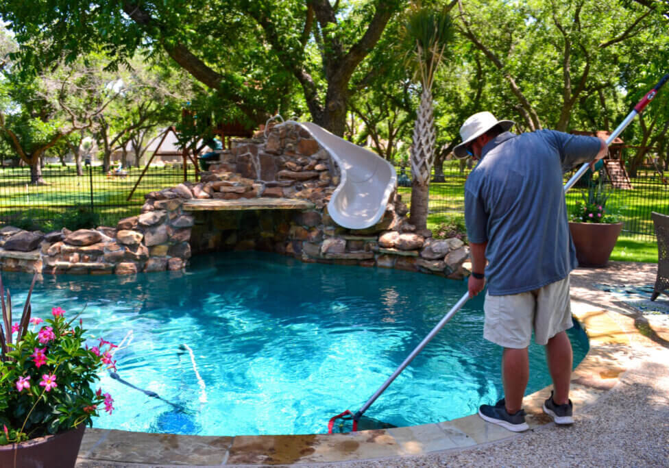 Professional from Emerald Custom Pools using a net while cleaning a pool.